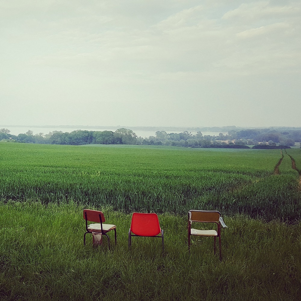 Bild von 3 Stühlen vor einem grünen Getreidefeld